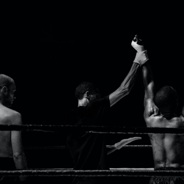grayscale photography of man holding boxer s hand inside battle ring